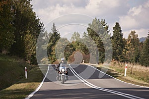 Biker in black leather outfit driving modern powerful motorcycle along sunny road on summer day.