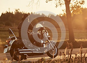 Biker in black leather outfit driving modern powerful motorcycle along sunny road on summer day.