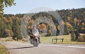 Biker in black leather outfit driving modern powerful motorcycle along sunny road on summer day.