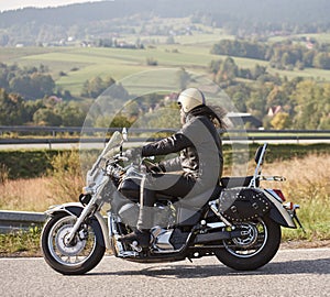 Biker in black leather outfit driving modern powerful motorcycle along sunny road on summer day.