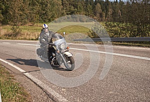 Biker in black leather outfit driving modern powerful motorcycle along sunny road on summer day.