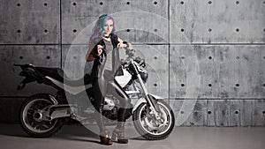 Biker chick in front of motorcycle. Beautiful and pert young woman in leather clothes