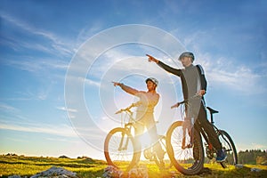 Biker couple with mountain bike pointing in distance at countryside