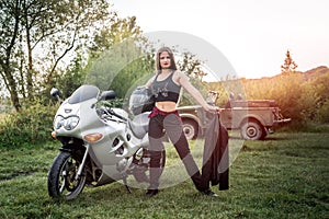 Biker girl holding leather jacket near motorcycle outside