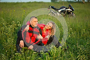 Biker girl and man sitting on the grass near a