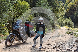 Biker girl in special motorcycle outfit, protection, knee pads and turtleneck. White helmet. Stands next to a long-distance