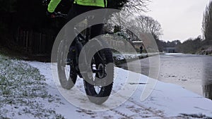 Biker in high-vis jacket cycles on canal towpath after winter snowfall