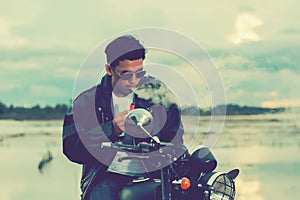 Biker man standing smokes with his motorbike beside the natural lake and beautiful, enjoying freedom and active lifestyle, having