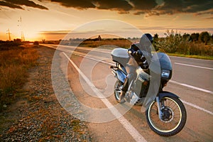 Biker and motorcycle on road at sunset