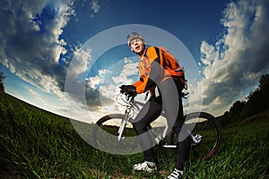 Biker in orange jersey riding on green summer field