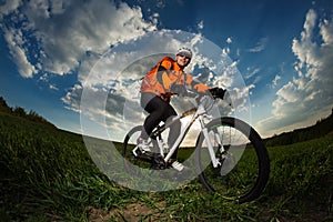 Biker in orange jersey riding on green summer field