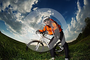 Biker in orange jersey riding on green summer field