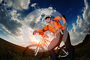 Biker in orange jersey riding on green summer field