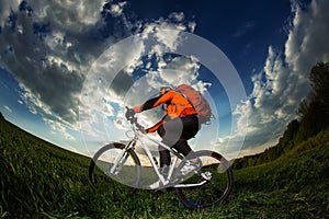 Biker in orange jersey riding on green summer field