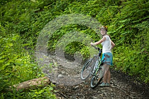 Biker pushes bicycle up in the green forest