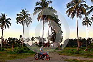 Biker with raised hand on a background of sunset in the tropics