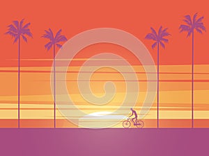 Biker riding bicycle at sunrise or sunset on the beach with palm trees in background. Symbol of active, healthy, sport