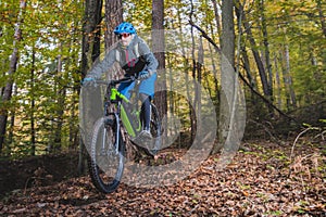 Biker riding downhill with a modern electric bicycle or mountain bike in autumn or winter setting in a forest. Modern e-cyclist in