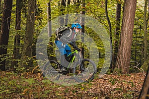 Biker riding uphill with a modern electric bicycle or mountain bike in autumn or winter setting in a forest. Modern e-cyclist in