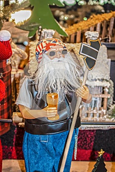 Biker Santa figure with sunglasses and a beer holding sign in front of jumble of other Christmasy items