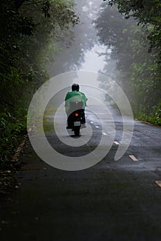 biker wearing plastic raincoat riding on foggy mountain road at khao yai national park thailand