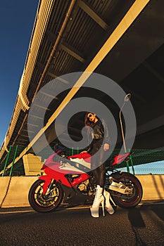 Biker Woman on motorcycle against bridge. Young brutal cute girl wear black leather jacket and sunglasses