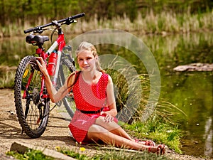 Bikes cycling girl sits near bicycle on shore into park.