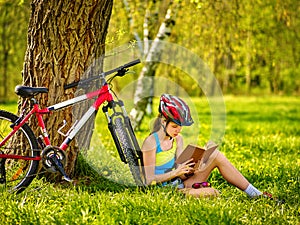 Bikes cycling girl wearing helmet read book on rest near bicycle.