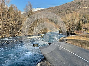 biking road at the edge of a river flowing in an alpine valley destroy