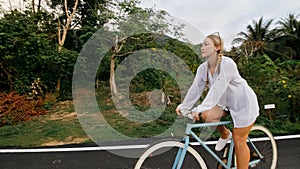 Biking road trip. The woman on blue bike in white clothes on forest road. The girl ride on bicycle. Cycling Cycle Fix