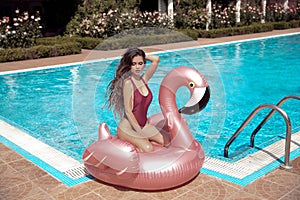 bikini girl model enjoying on inflatable giant pink flamingo pool float mattress in fashion swimwear. Attractive tanned woman