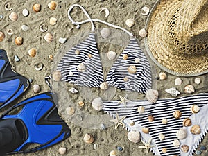 Bikini set, swim fins and straw hat on beach sand