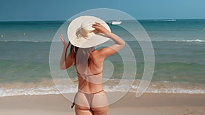Bikini woman wearing hat woman running into sea hat whisked away by wind. Running into ocean symbolizes carefree joy of