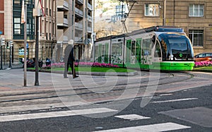 BILBAO, SPAIN-DECEMBER 19, 2021 : Elderly people walking near Euskotren city tram runs on tramway track. Modern transport in