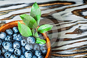 Bilberries green leaves in round wooden bowl on wood board