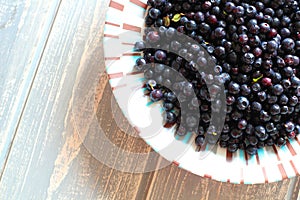 Bilberries in white plate on wooden grey desk.