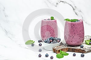 Bilberry smoothie yogurt, fresh blueberries in glass with mint leaf and raw beeries on white background. Restaurant menu, dieting photo