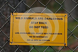 Bilingual warning sign near bear enclosure at zoo.