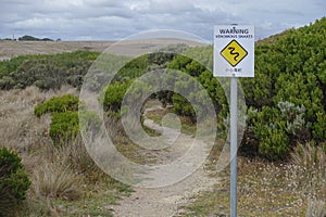 Bilingual warning signpost in English and Chinese of venomous snake activity on a footpath near Great Ocean Road of Australia.