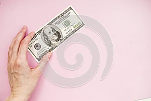 Bill in hand on a pink background. 100 dollars. Money