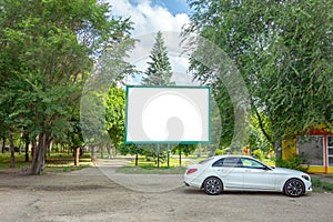 Billboard with copy space in park. Blank poster board among green trees and under blue sky. Banner panel with white background to