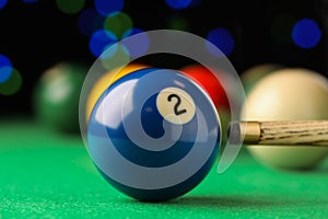 Billiard ball with number 2 and cue on green table, closeup