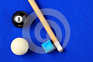 Billiard balls, cue and chalk in a blue pool table.