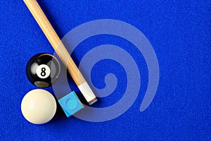 Billiard balls, cue and chalk in a blue pool table.