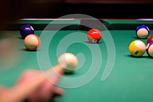 billiard balls in a green billiard table. Blurred hand with cue pointing at billiard ball at table