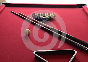 Billiard balls on a red pool table with two cues, a black ball rack and a white cue ball