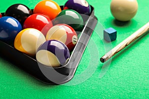 Billiard balls in triangle rack, cue and chalk on green table, closeup