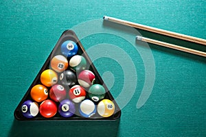 Billiard balls in triangle rack with cues on table