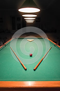 Billiard table with balls and cues in the light of the lamps