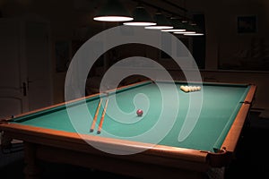 Billiard table with balls and cues in the light of the lamps